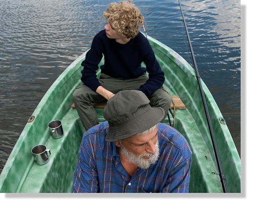 An elderly man and young child sitting in a row boat on the water